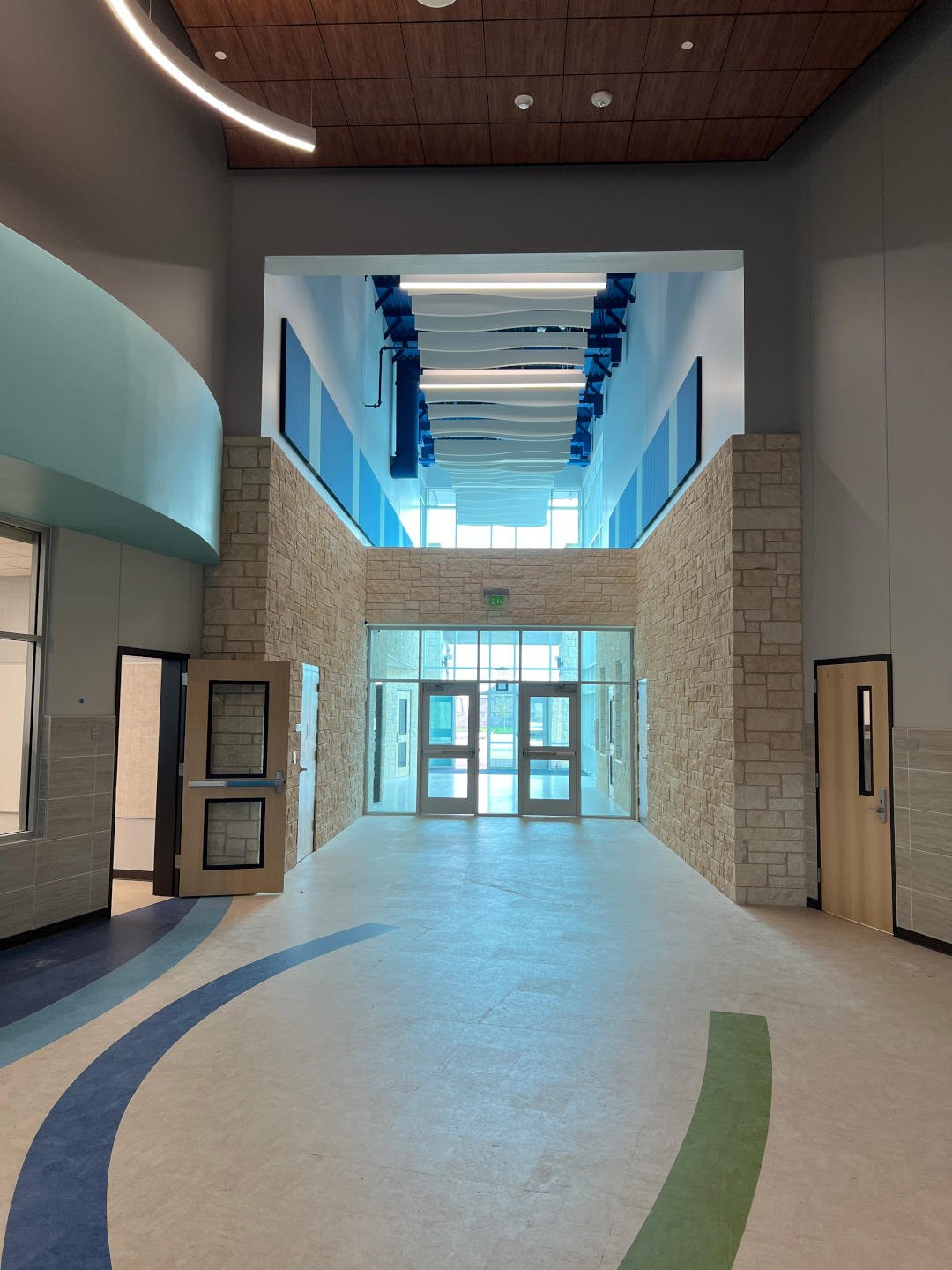 Pflugerville ISD – Elementary School #23  Pflugerville ISD’s Elementary School #23 consists of new construction of a two-story, 116,000 SF elementary building on 23.44 acres of undisturbed land.  Public work included an extension of Hidden Lake Drive and a collector road to be deeded over to the City of Pflugerville.  The building consists of classrooms for K-5 with multiple collaborative learning areas and media center.  Exterior building façade includes brick, stone, metal panel, and glass curtainwall.  Site work includes car rider drop-off, two detention ponds, multiple aluminum canopies, covered basketball court, playgrounds with poured in place surfacing, tensioned shade structures, outdoor learning spaces, and walking track.  Back to Portfolio 